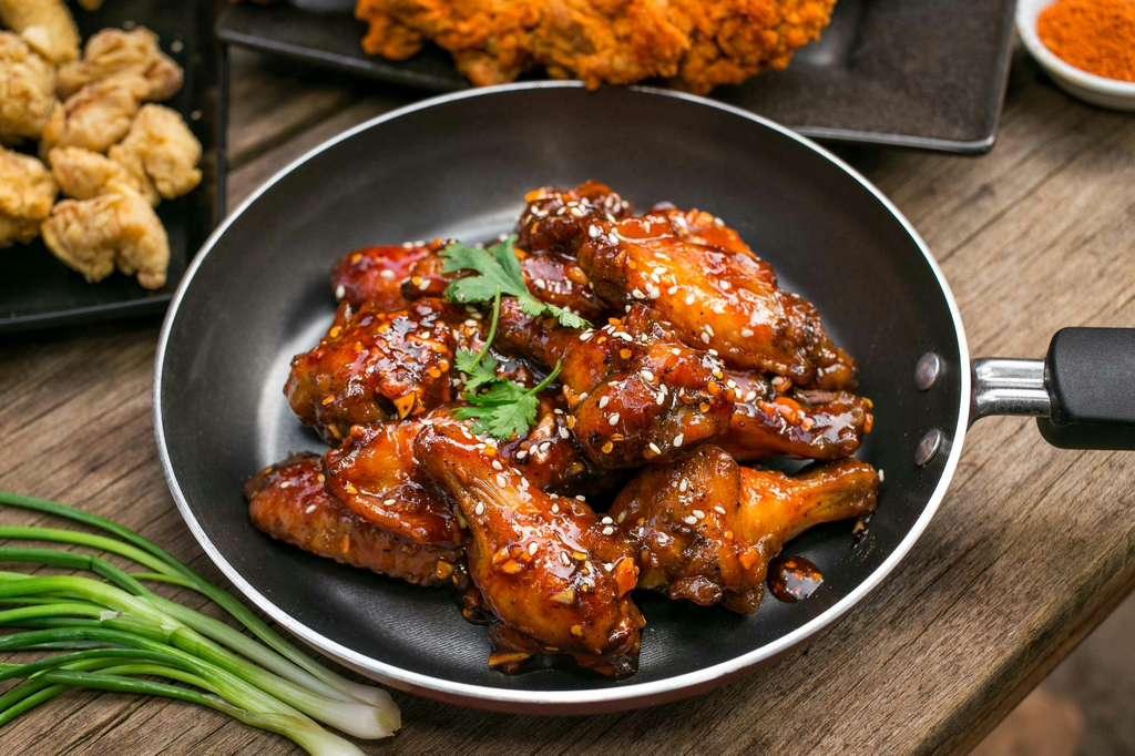 Baked chicken wings with a spicy sauce in a black skillet on a wooden table - Jerk Fry City