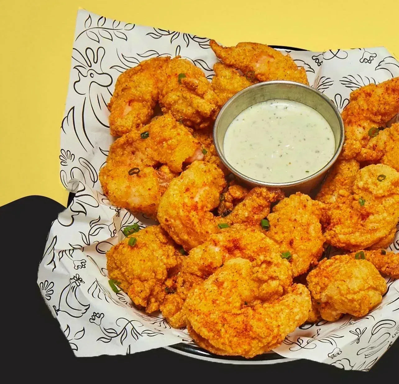 Bowl of fried shrimp with a side of sauce on a decorative paper liner against a yellow background - Jerk Fry City