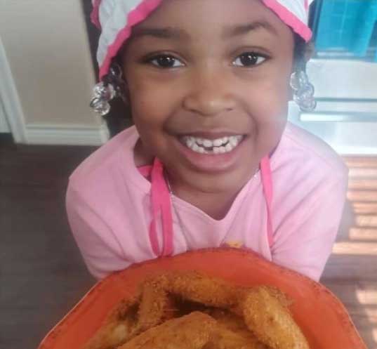 Child in pink outfit holding a bowl indoors