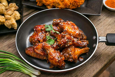 Baked chicken wings with a spicy sauce in a black skillet on a wooden table - Jerk Fry City