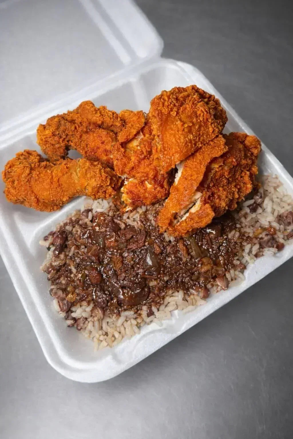 Fried chicken and rice in a takeout container on a gray surface - Jerk Fry City