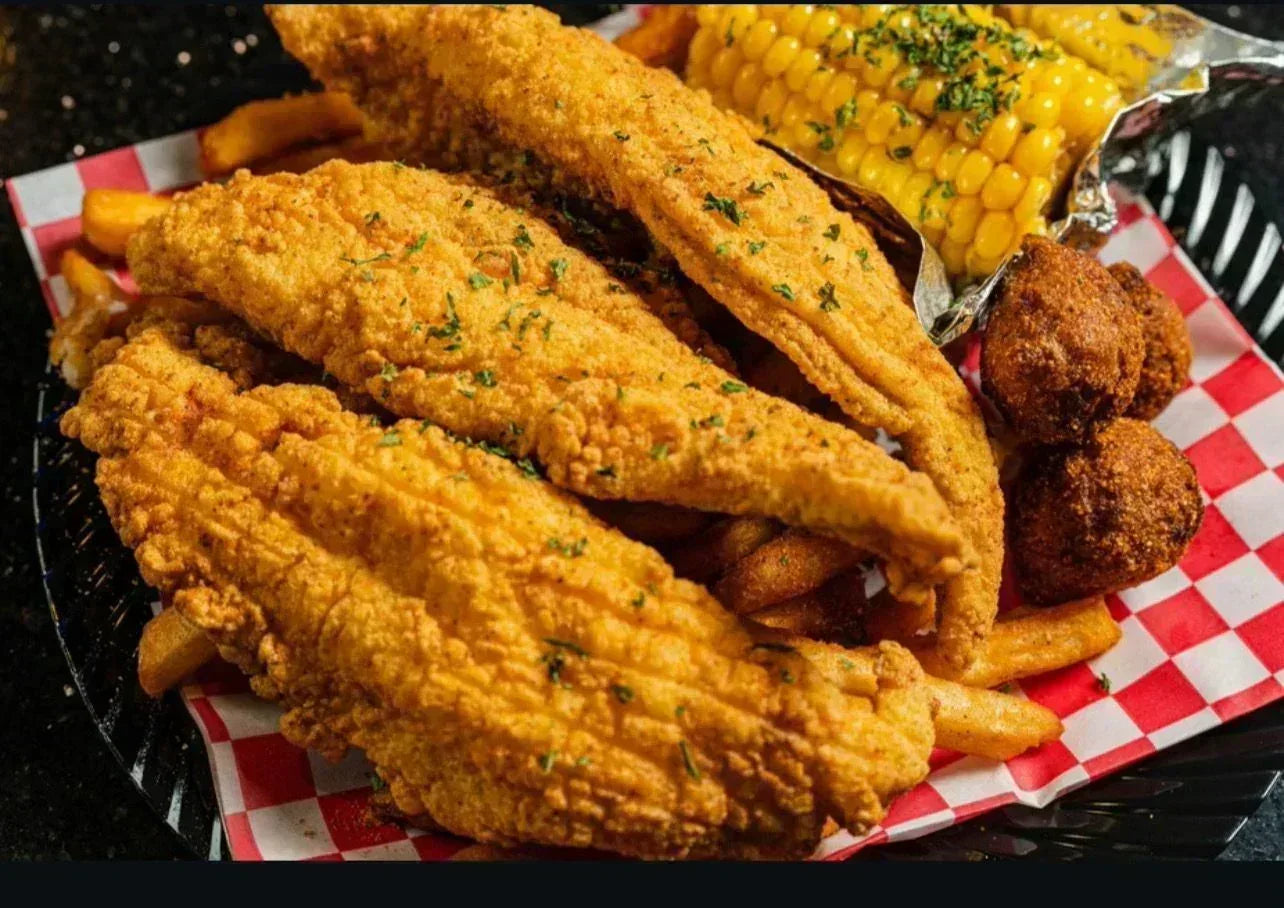 Fried chicken, corn on the cob, and hush puppies on a checkered paper-lined plate - Jerk Fry City