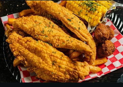 Fried chicken, corn on the cob, and hush puppies on a checkered paper-lined plate - Jerk Fry City