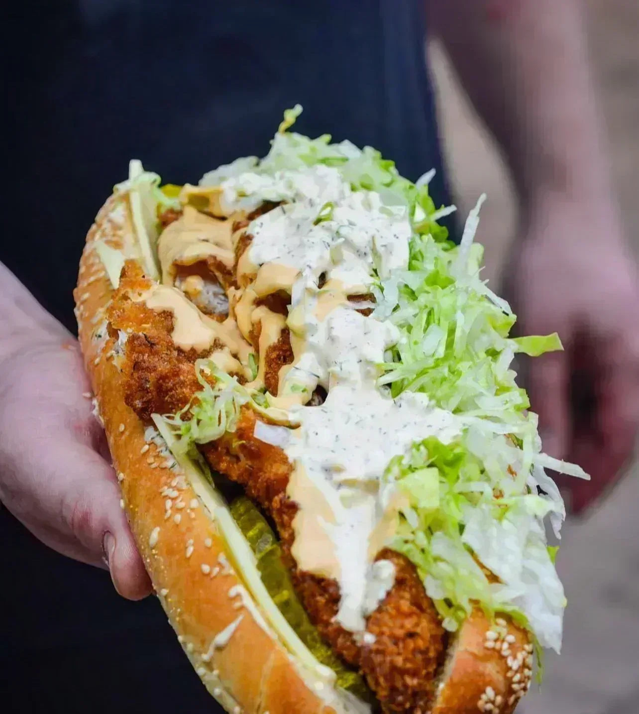 Hand holding a sandwich with fried chicken, coleslaw, and pickles - Jerk Fry City